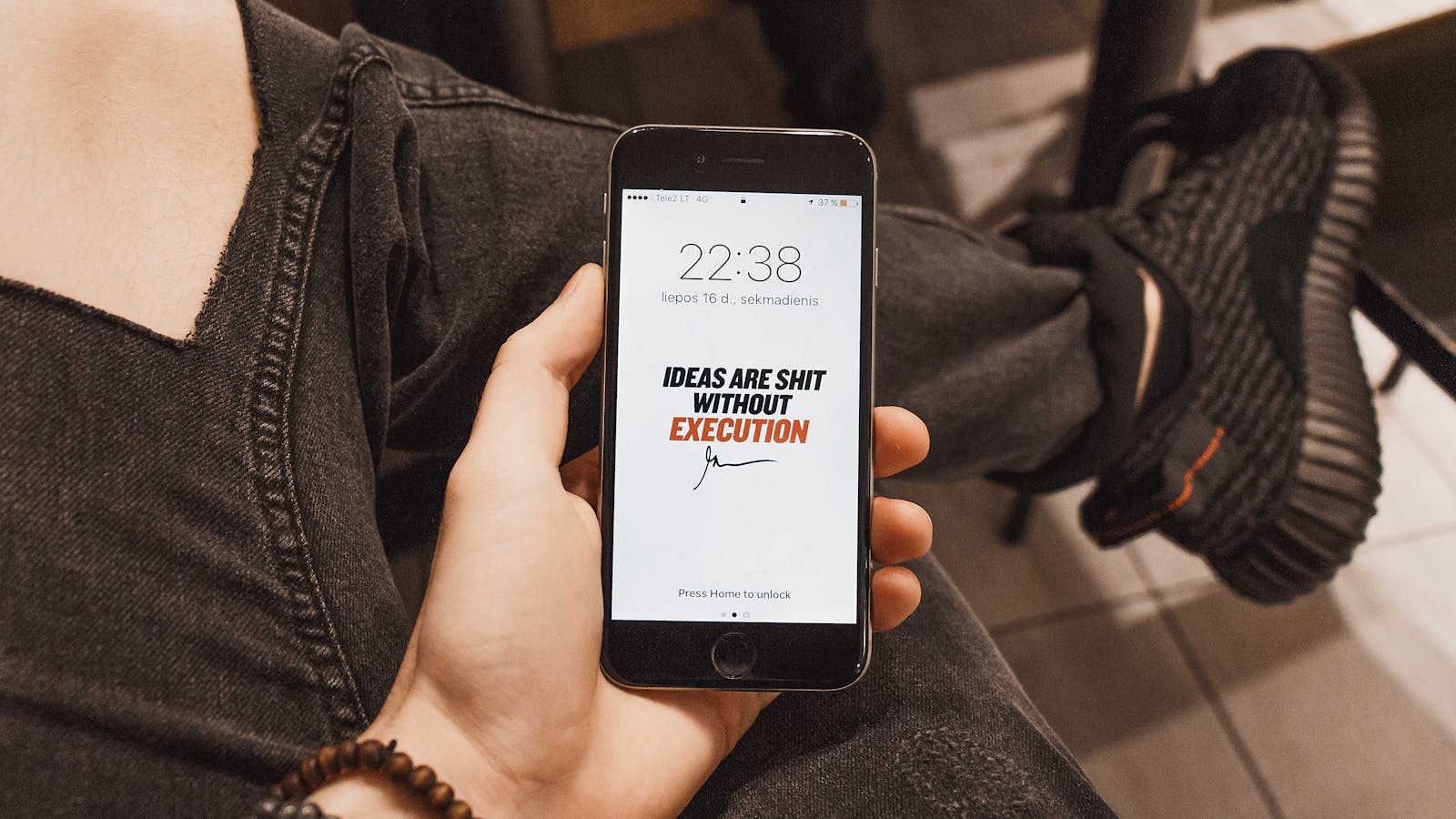 Hand holding iPhone displaying motivational quote. Casual setting with sneakers visible.