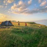toddler walking on green grass with set-up tent during golden hour